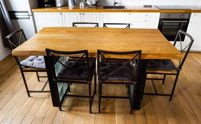A big wooden dining table with glass blocks and metal wicker chairs and pillows in modern scandinavian an eat-in kitchen, against bright white furnitures, appliances and light wood floor